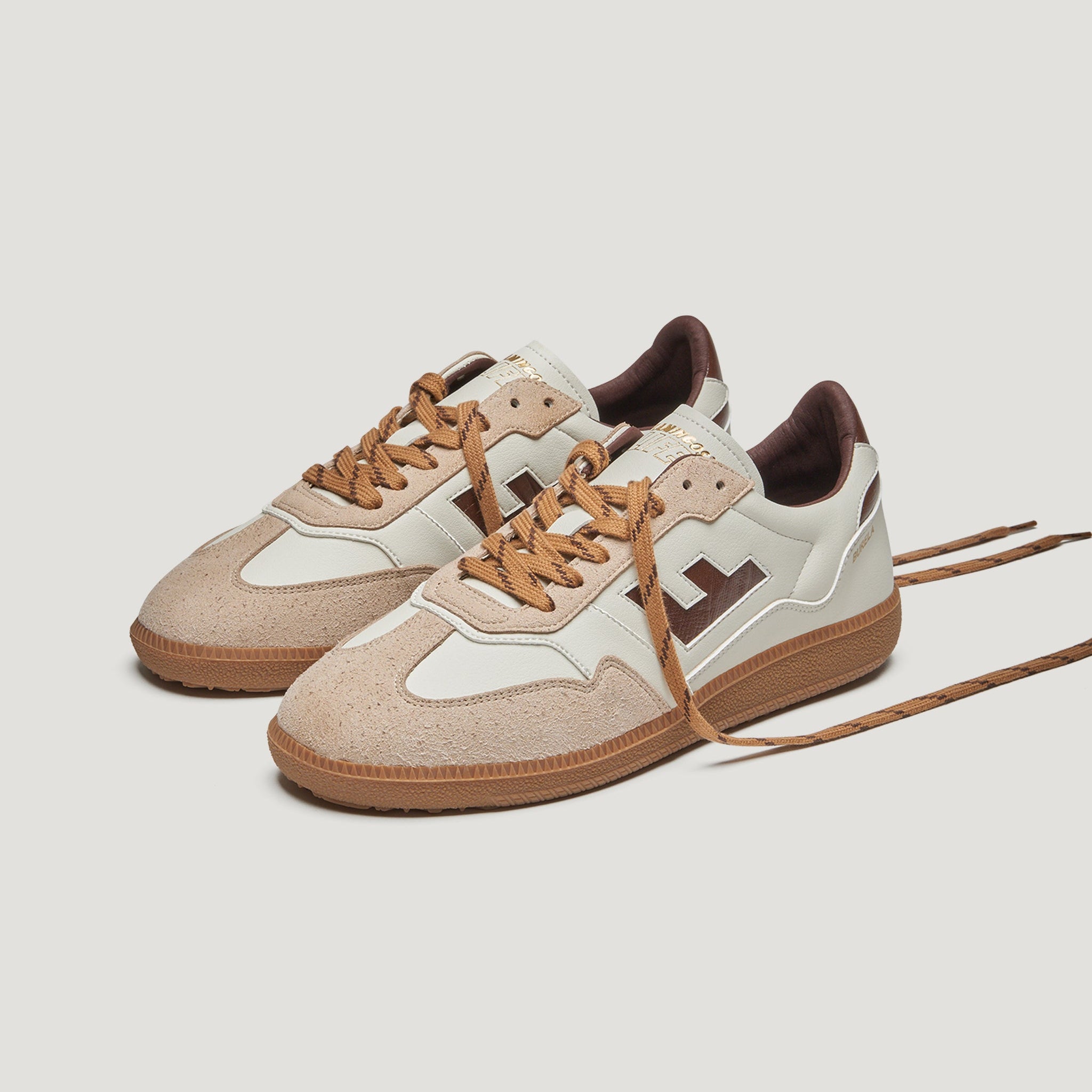 Ein Paar beige- und hellbraune Sneakers mit braunen Schnürsenkeln, Wildleder- und Ledereinsätzen, einem seitlichen Logo und Gummisohlen auf einem schlichten weißen Hintergrund.