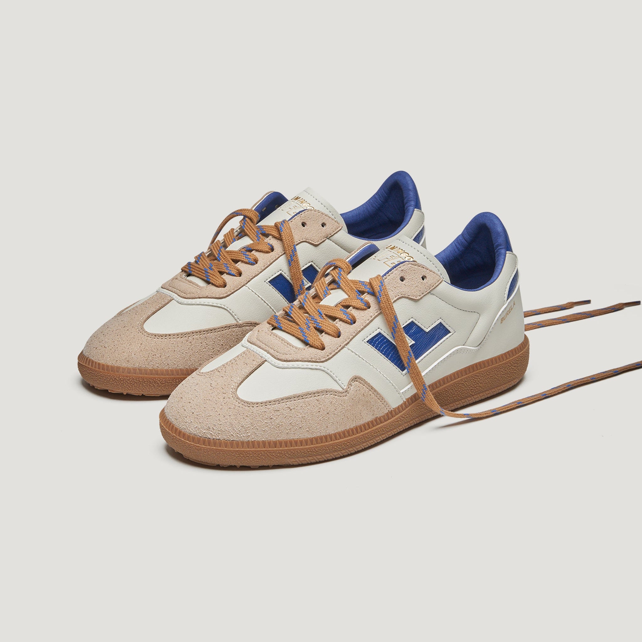 Ein Paar beigefarbene und weiße Turnschuhe mit braunen Sohlen, blauen Akzenten und braunen Schnürsenkeln auf einem schlichten weißen Hintergrund.