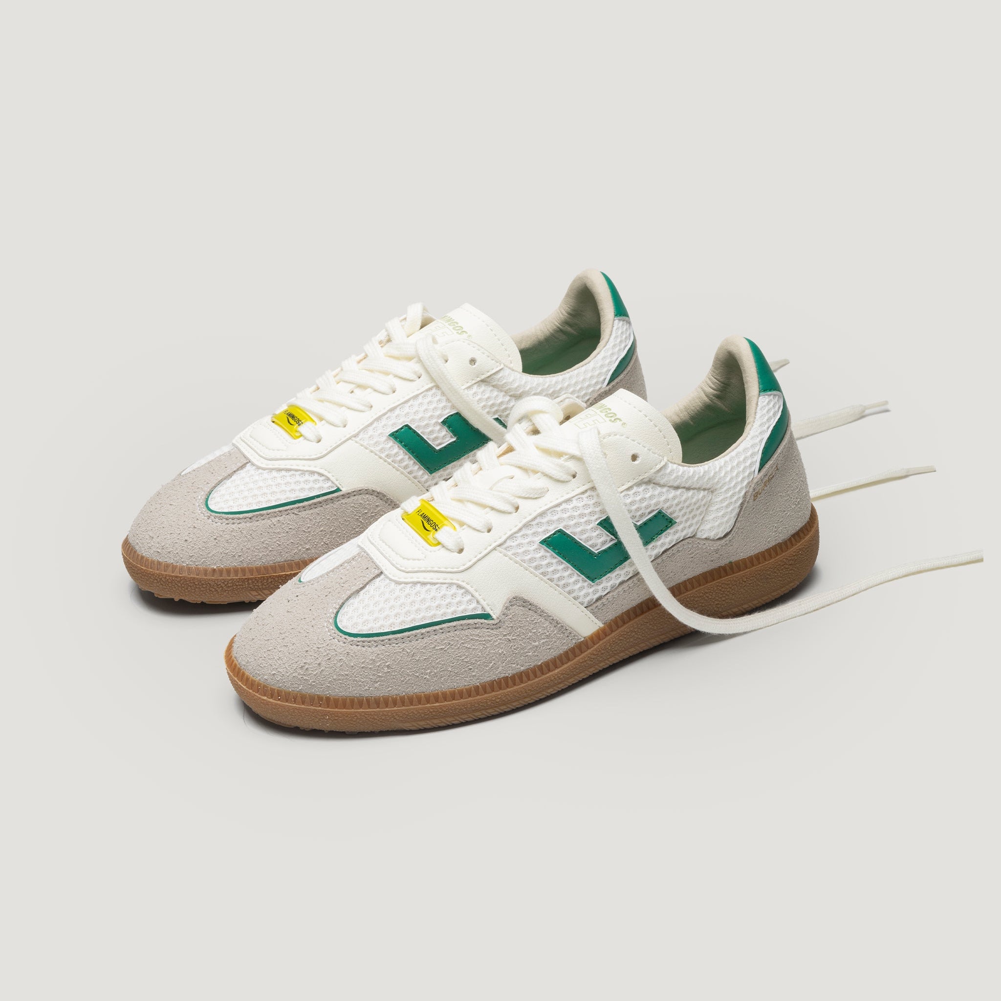 Ein Paar stylische Sneaker mit weißem Mesh, beigen Wildleder-Overlays, grünen Akzenten, Gummisohlen und weißen Schnürsenkeln vor einem schlichten, hellen Hintergrund.