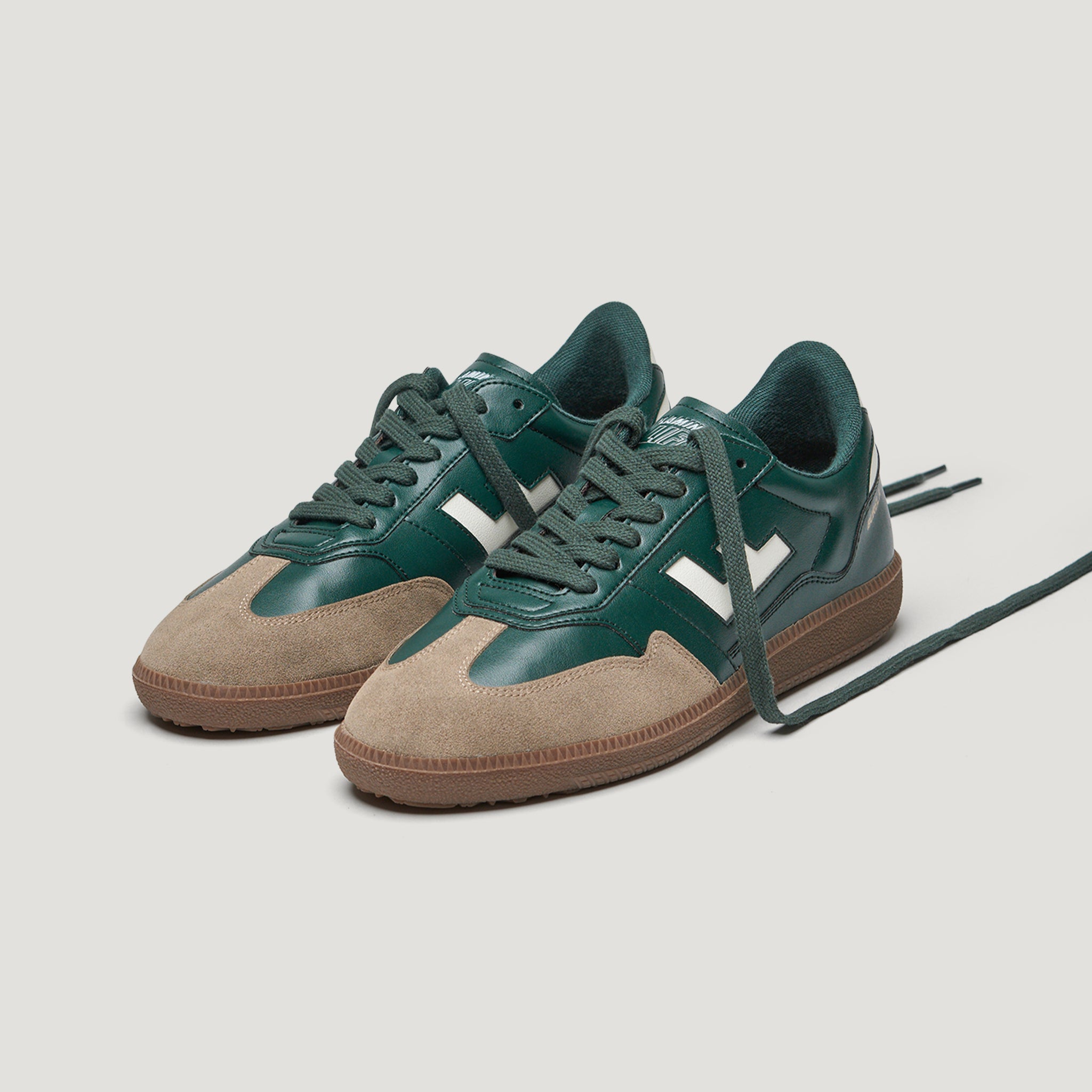 Grüne Turnschuhe mit beigen Wildledereinsätzen und brauner Sohle, auf hellem Hintergrund.