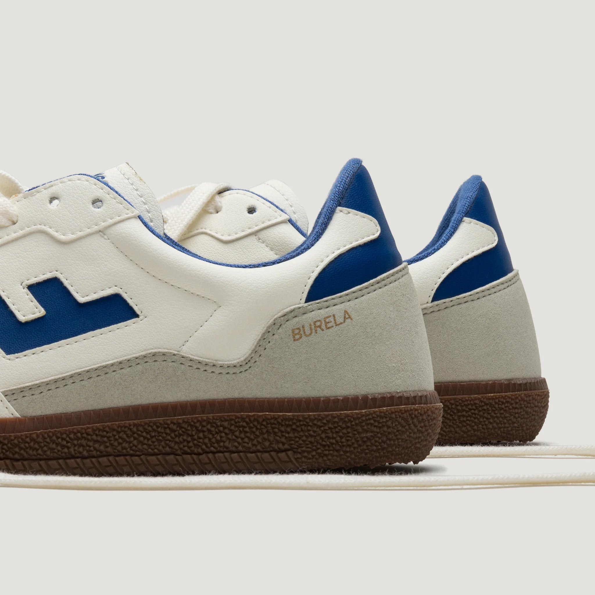 Weiße Sneaker mit blauen Details und brauner Sohle, seitlich fotografiert.