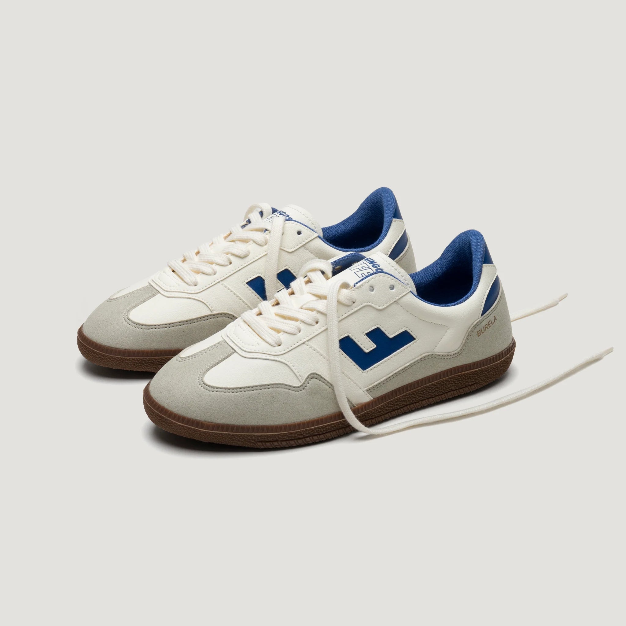 Weiß-graue Turnschuhe mit blauen Details und brauner Sohle, auf einem neutralen Hintergrund abgebildet.