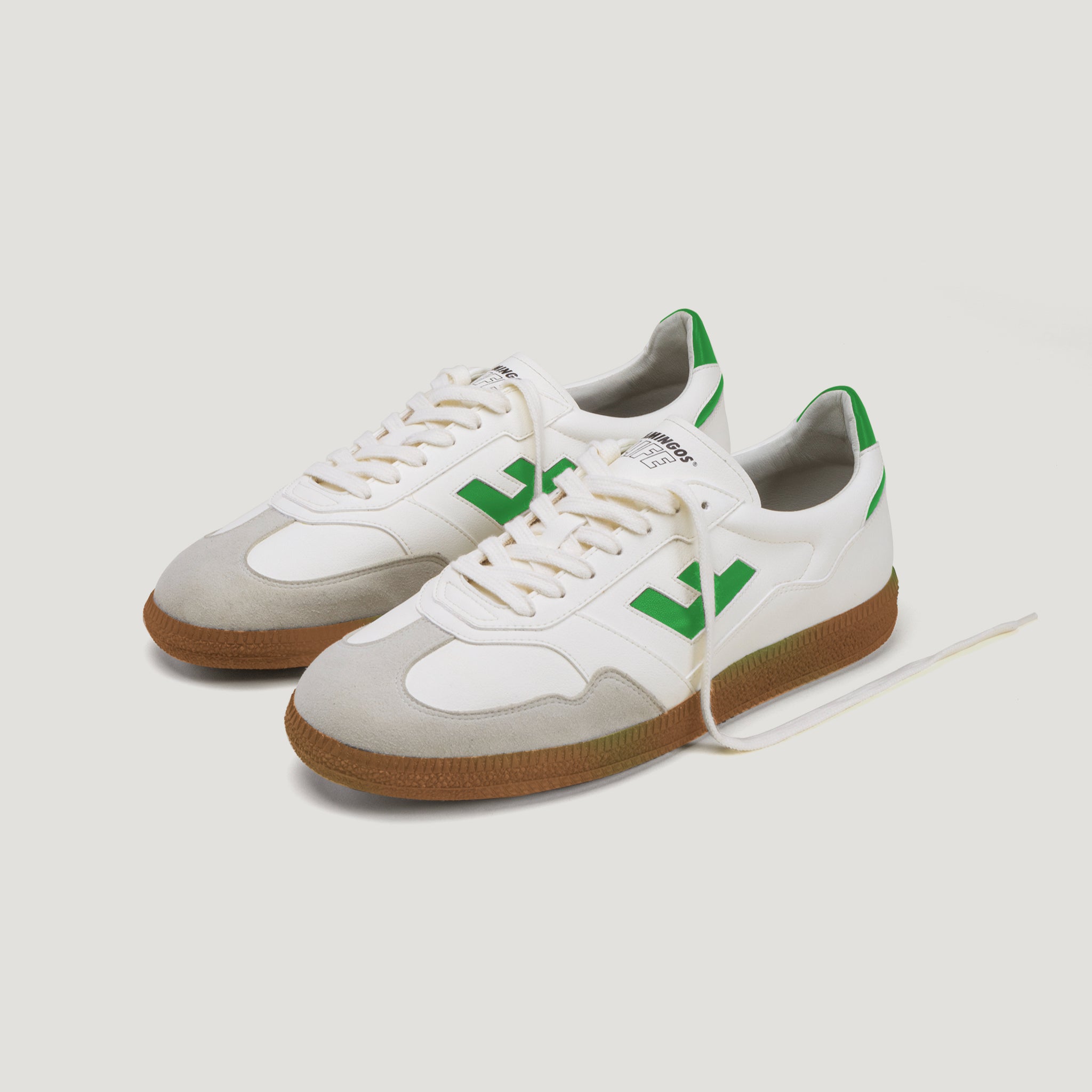Weiße Turnschuhe mit grünen Details und brauner Sohle auf weißem Hintergrund.