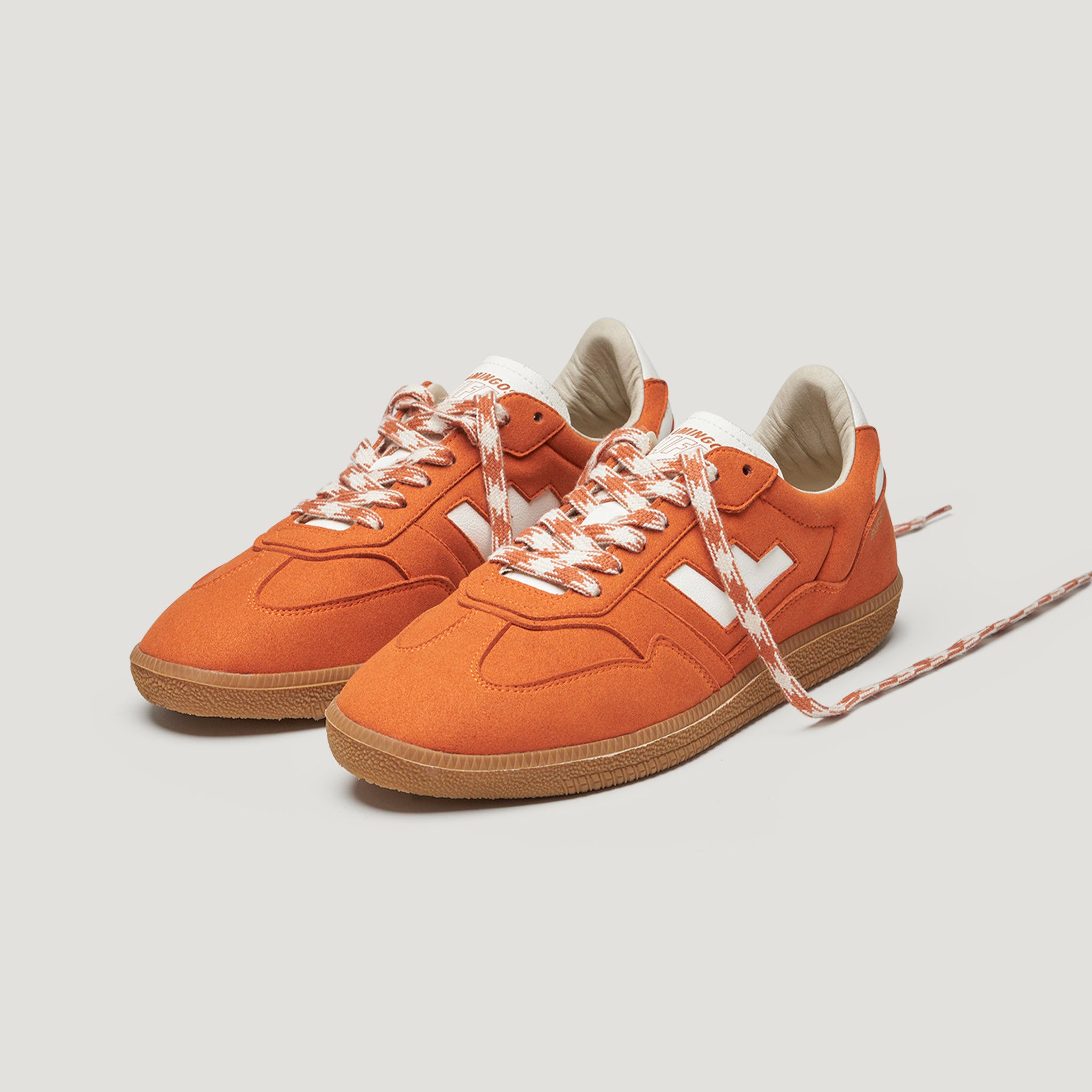 Orange Sneakers mit weißen Details und gemusterten Schnürsenkeln auf weißem Hintergrund.
