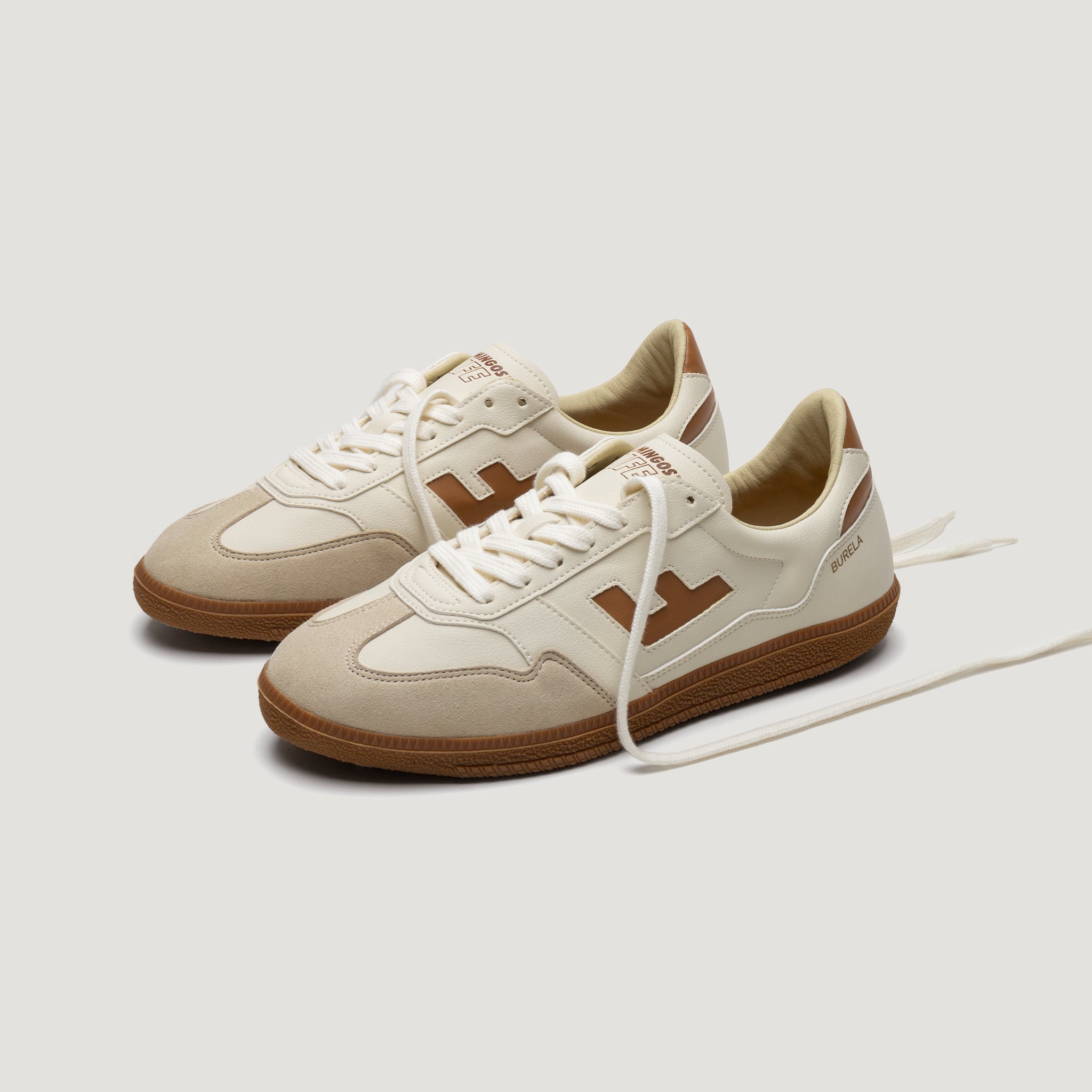 Beige-weiße Turnschuhe mit braunen Details und brauner Sohle auf weißem Hintergrund.
