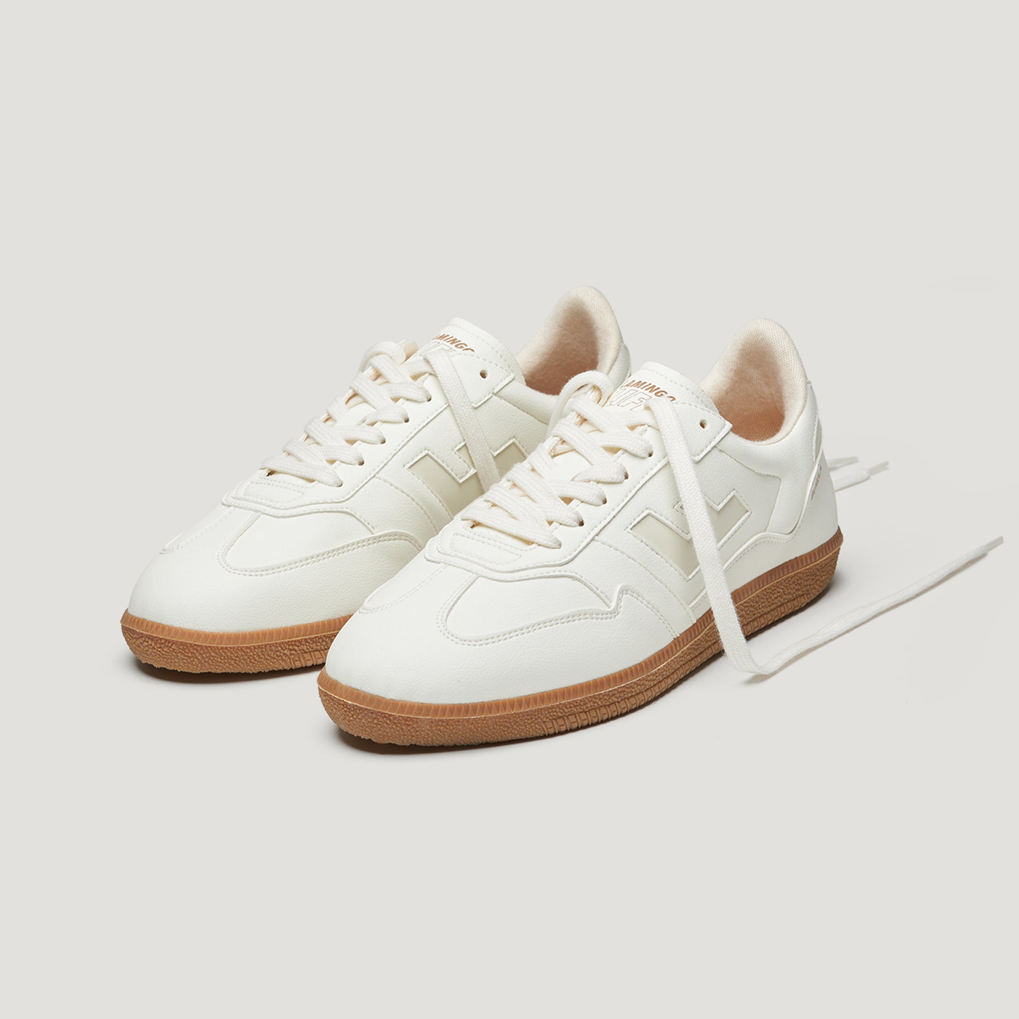 Weiße Sneaker mit brauner Sohle und weißen Schnürsenkeln, auf hellem Hintergrund.