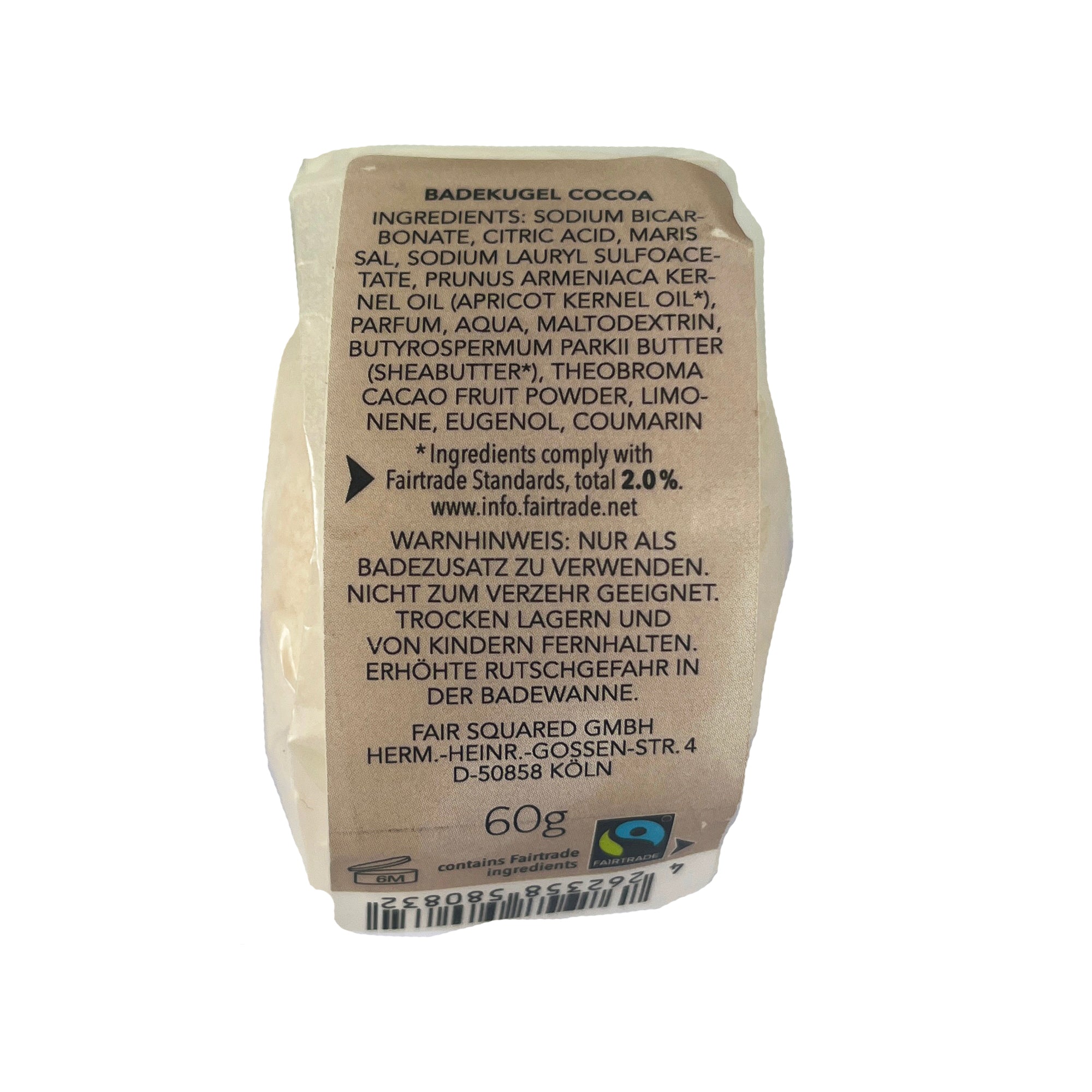 Eine braune Badebombe mit einem Etikett, auf dem die Zutaten, Fairtrade-Informationen und die Adresse des Herstellers in deutscher Sprache aufgeführt sind. Die Badebombe wiegt 60 g und ist mit einem Fairtrade-Zertifizierungslogo versehen.