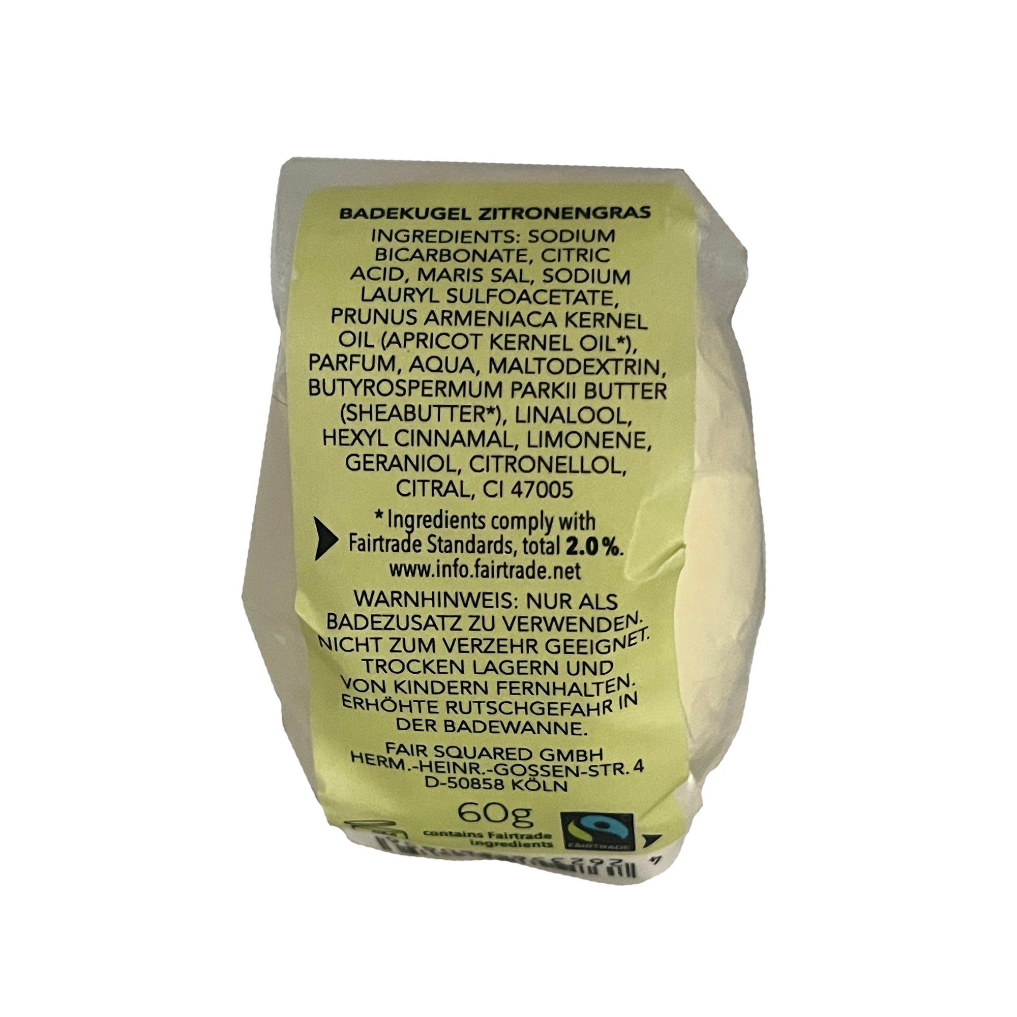 Eine Nahaufnahme eines zitronengelben Badebomben-Etiketts mit Zutaten, Fairtrade-Zertifizierung, Gewicht (60 g) und Herstellerangaben in deutscher Sprache. Auf dem Etikett sind der Duft von Zitronengras und Anwendungshinweise angegeben.