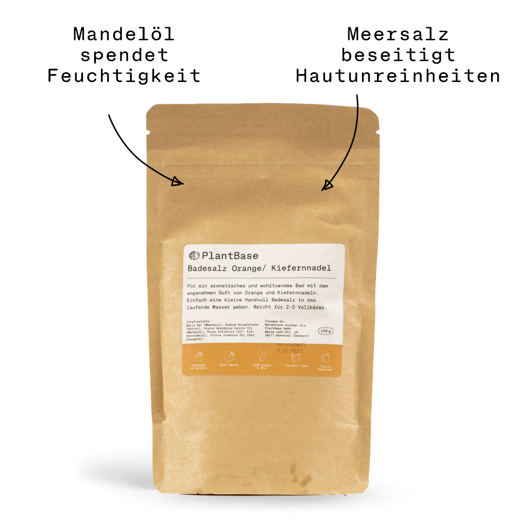 Ein brauner Kraftpapierbeutel mit einem Etikett mit der Aufschrift "PlantBase Badesalz Orange/Kiefernnadel". Das Etikett enthält Produktangaben und Symbole, die auf natürliche Inhaltsstoffe und eine umweltfreundliche Verpackung hinweisen. Der Beutel ist an der Oberseite verschlossen.