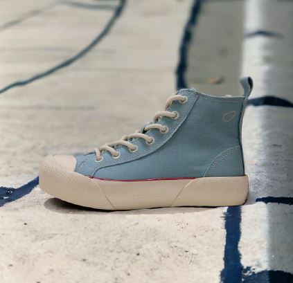 Blauer High-Top-Sneaker mit beiger Sohle auf einem weißen und blau gestreiften Untergrund.