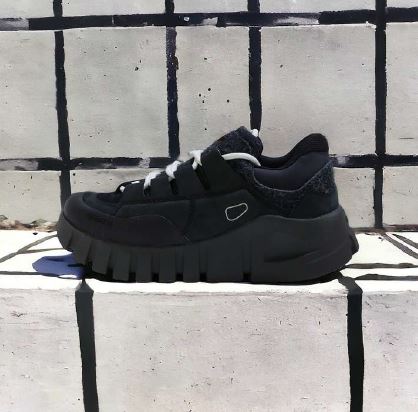 Schwarzer Sneaker mit dicker Sohle vor einer weiß-schwarz karierten Wand.