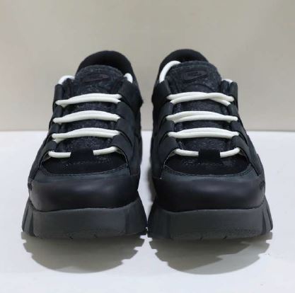 Schwarze Sneaker mit weißen Schnürsenkeln, frontal auf hellem Hintergrund fotografiert.