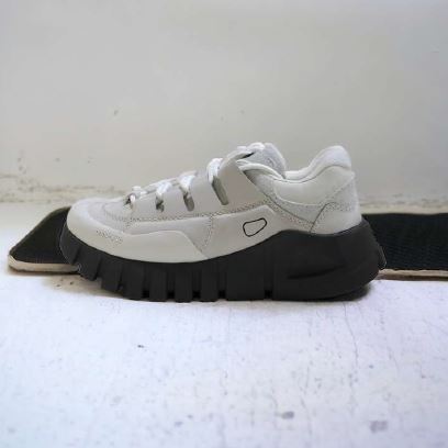 Weißen Sneaker mit dicker, schwarzer Sohle auf hellem Boden fotografiert.
