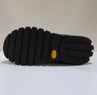 Schwarze Schuhsohle mit grobem Profil und gelbem Markenzeichen auf weißem Hintergrund.