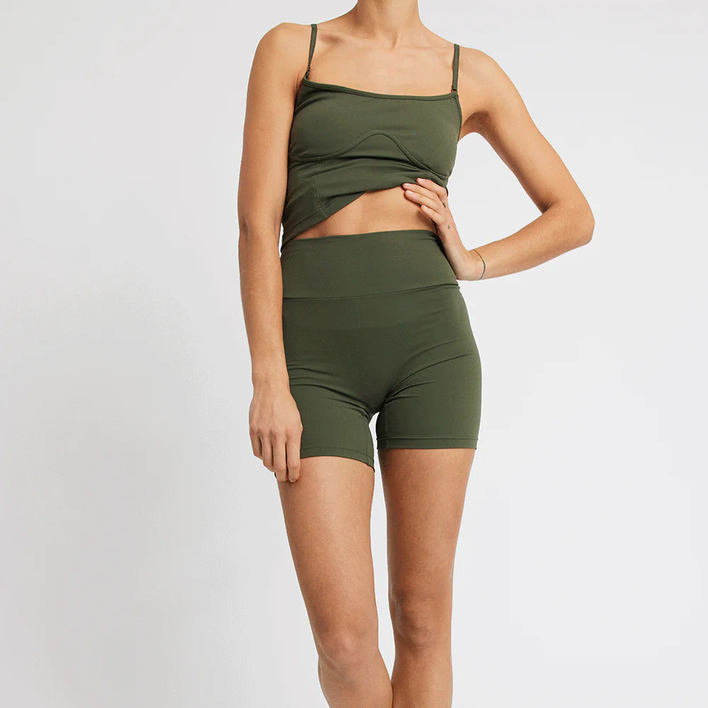 Person in grüner Sportbekleidung, bestehend aus engem Oberteil und Shorts, vor einem weißen Hintergrund.