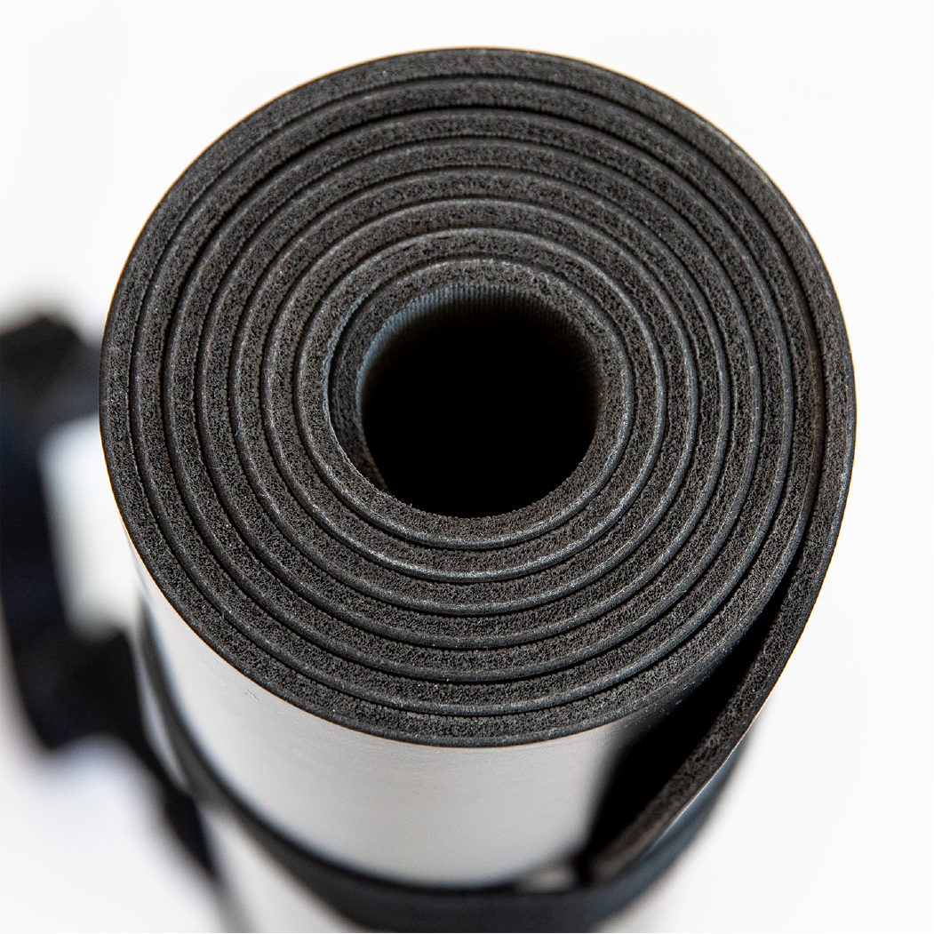 Zusammengerollte schwarze Yogamatte aus Schaumstoff auf weißem Hintergrund, von oben fotografiert.