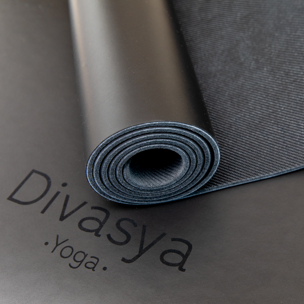 Aufgerollte schwarze Yogamatte mit der Aufschrift "Divasya Yoga" auf der Unterlage.