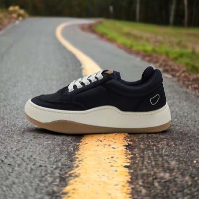 Schwarzer Sneaker mit weißen Schnürsenkeln liegt auf einer asphaltierten Straße mit gelber Mittelstreifenmarkierung.