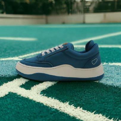 Blauer Sneaker mit weißer Sohle auf einem blauen Sportfeld platziert.