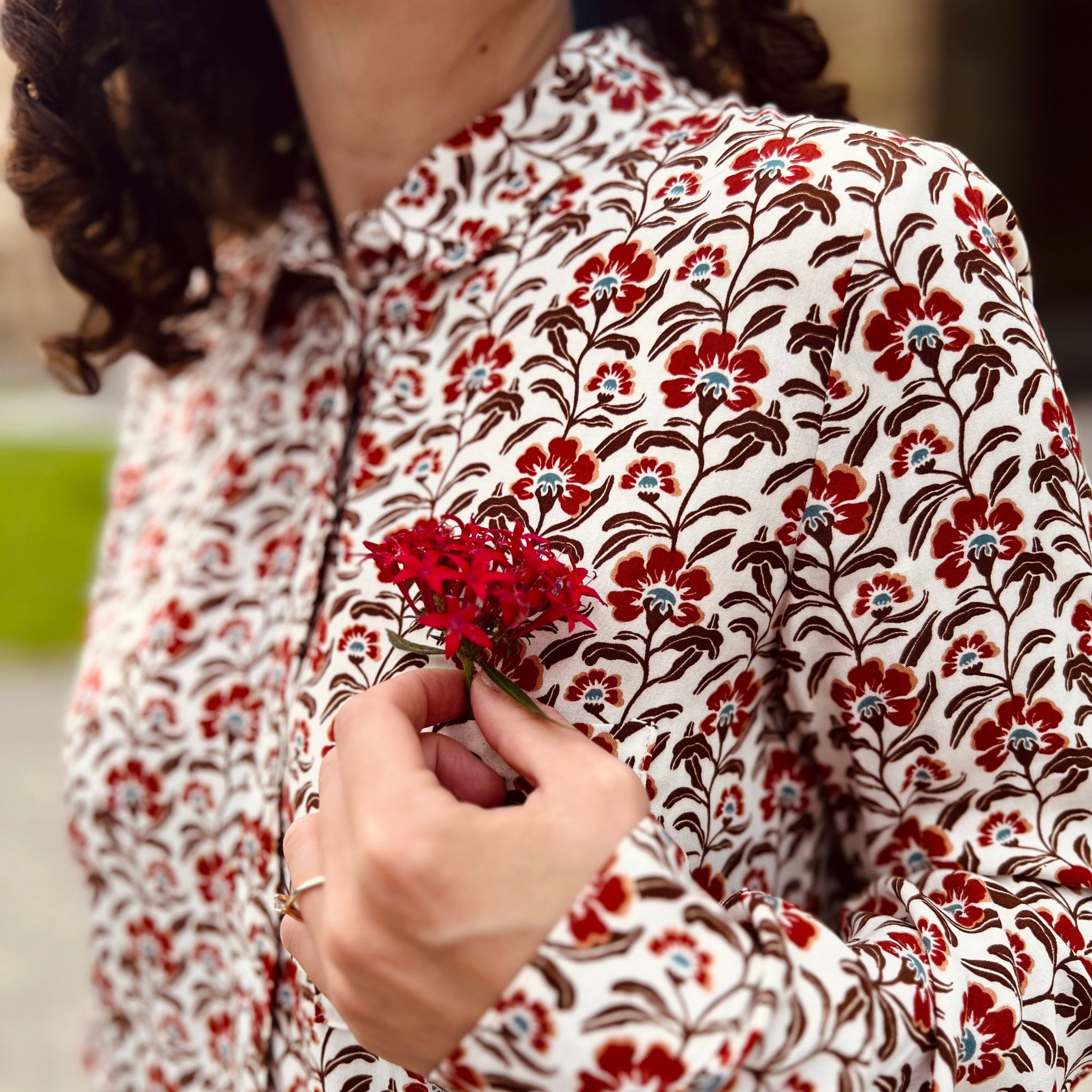 Person in floral patterned shirt holds a small red flower.