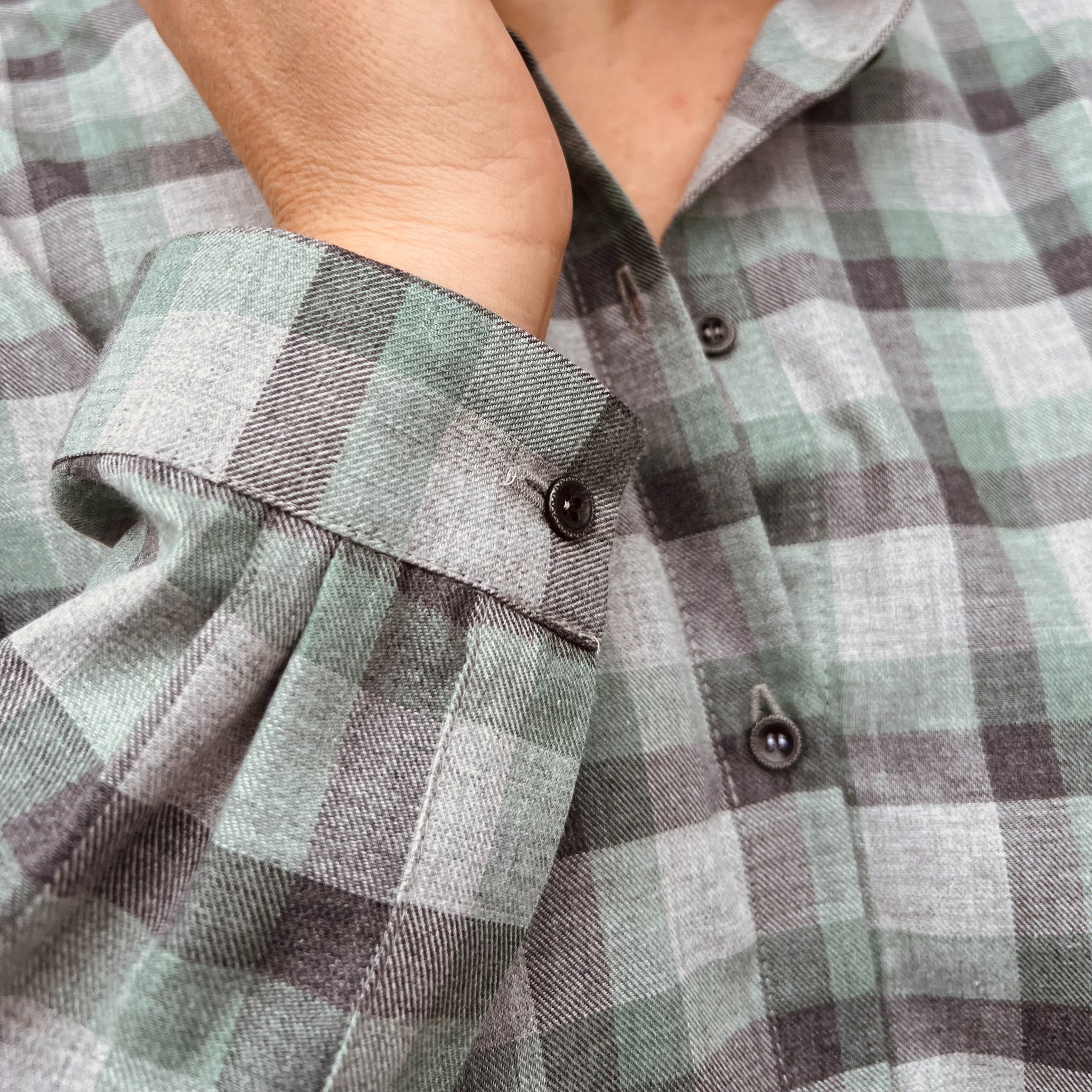 Nahaufnahme eines karierten Hemdes in Grün- und Grautönen mit einem hochgekrämpelten Ärmel.