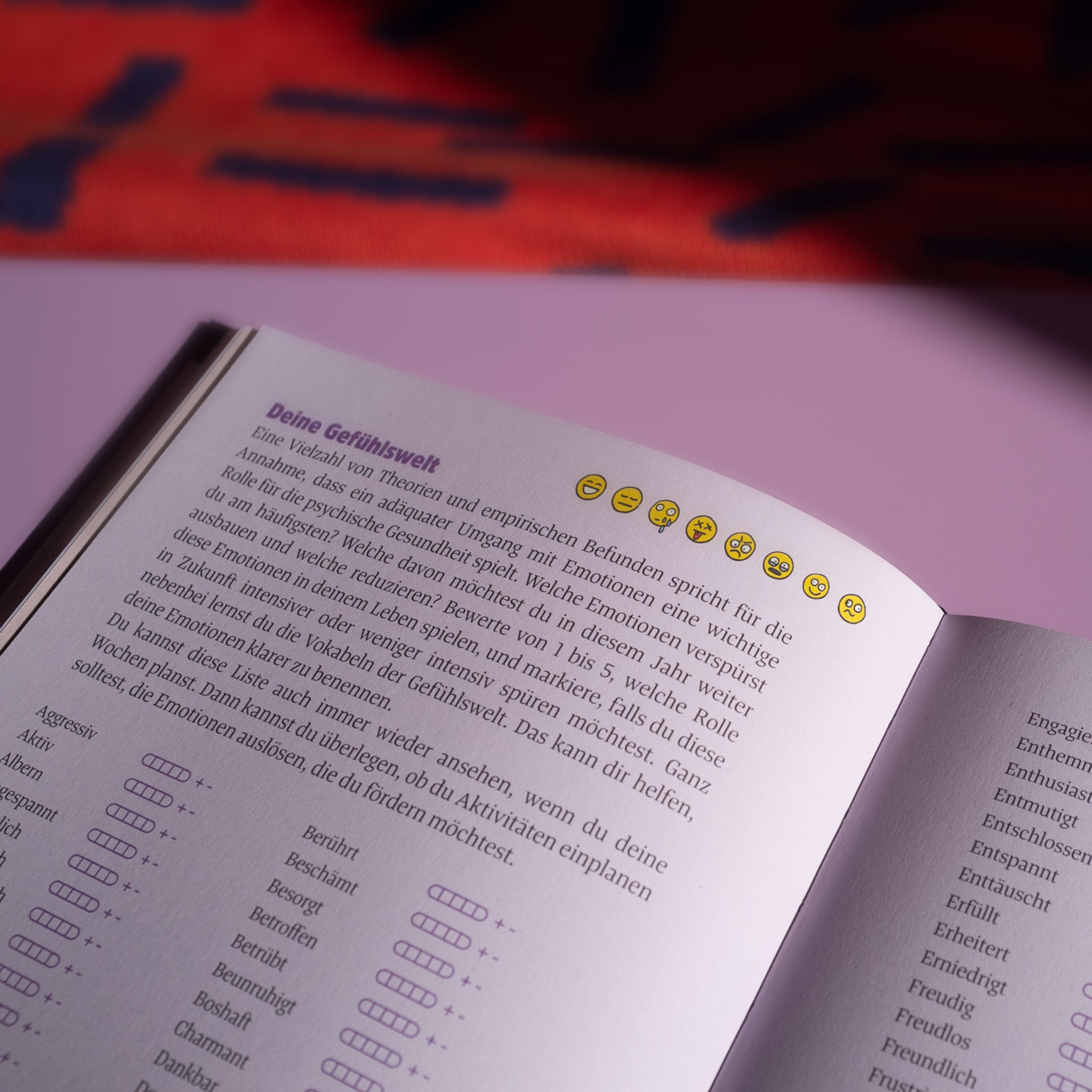 Eine Buchseite mit Text über Emotionen und kleinen Emoji-Symbolen am oberen Rand, auf einem rosa Hintergrund.