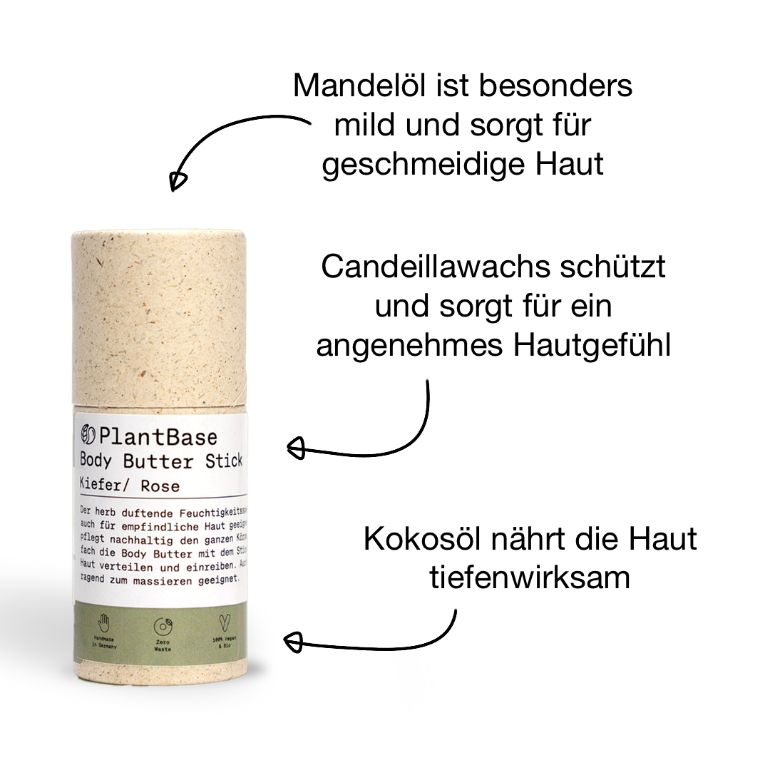 Eine zylindrische Papptube mit der Aufschrift PlantBase Body Butter Stick Kiefer/Rose und deutschem Text, mit grünem und weißem Design, steht aufrecht auf einem schlichten schwarzen Hintergrund.