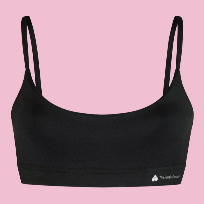 Schwarzer BH mit dünnen Trägern und kleinem Logo auf rosa Hintergrund.