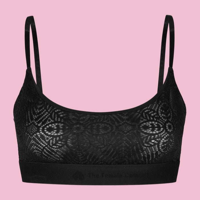 Schwarzes Spitzen-Bralette mit dünnen Trägern vor einem rosa Hintergrund.
