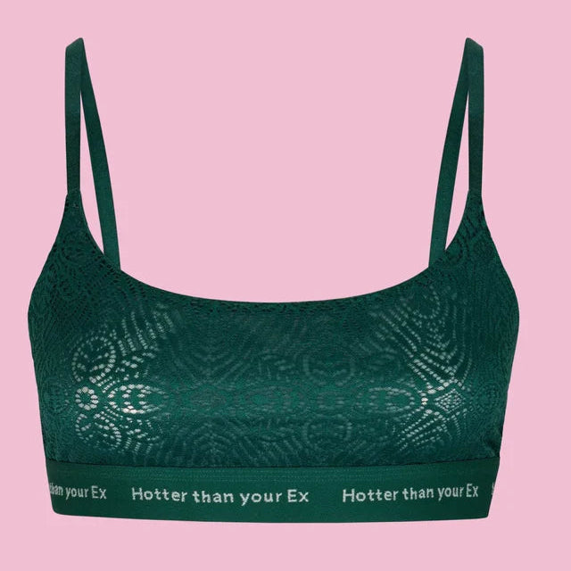 Ein dunkelgrüner Spitzen-Bralette mit dünnen Trägern und dem Schriftzug Hotter than your Ex auf dem Band vor einem rosa Hintergrund.