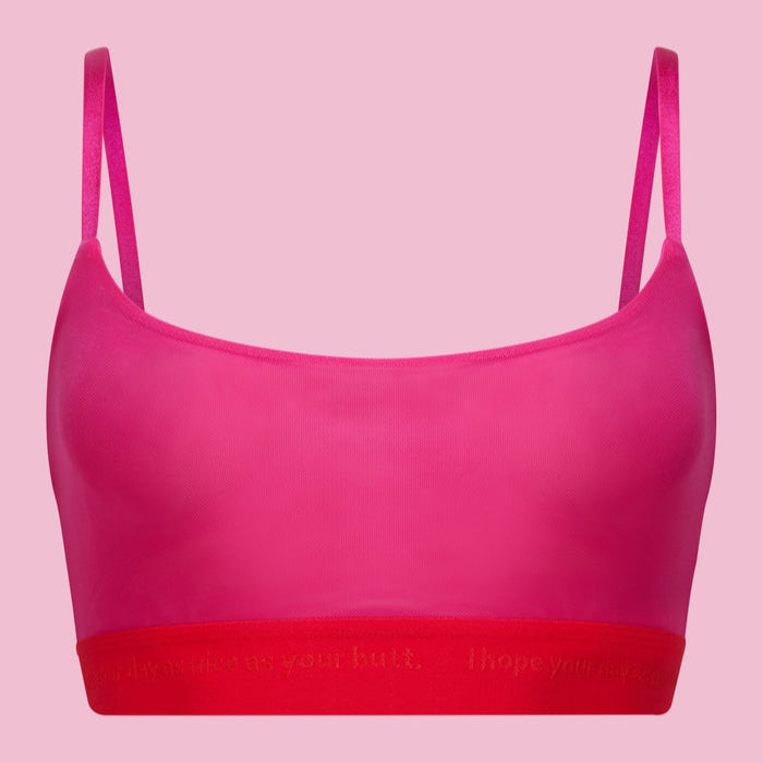 Pinkes, ärmelloses Crop-Top mit roten, elastischen Trägern und einem roten Bund vor einem passenden rosa Hintergrund.