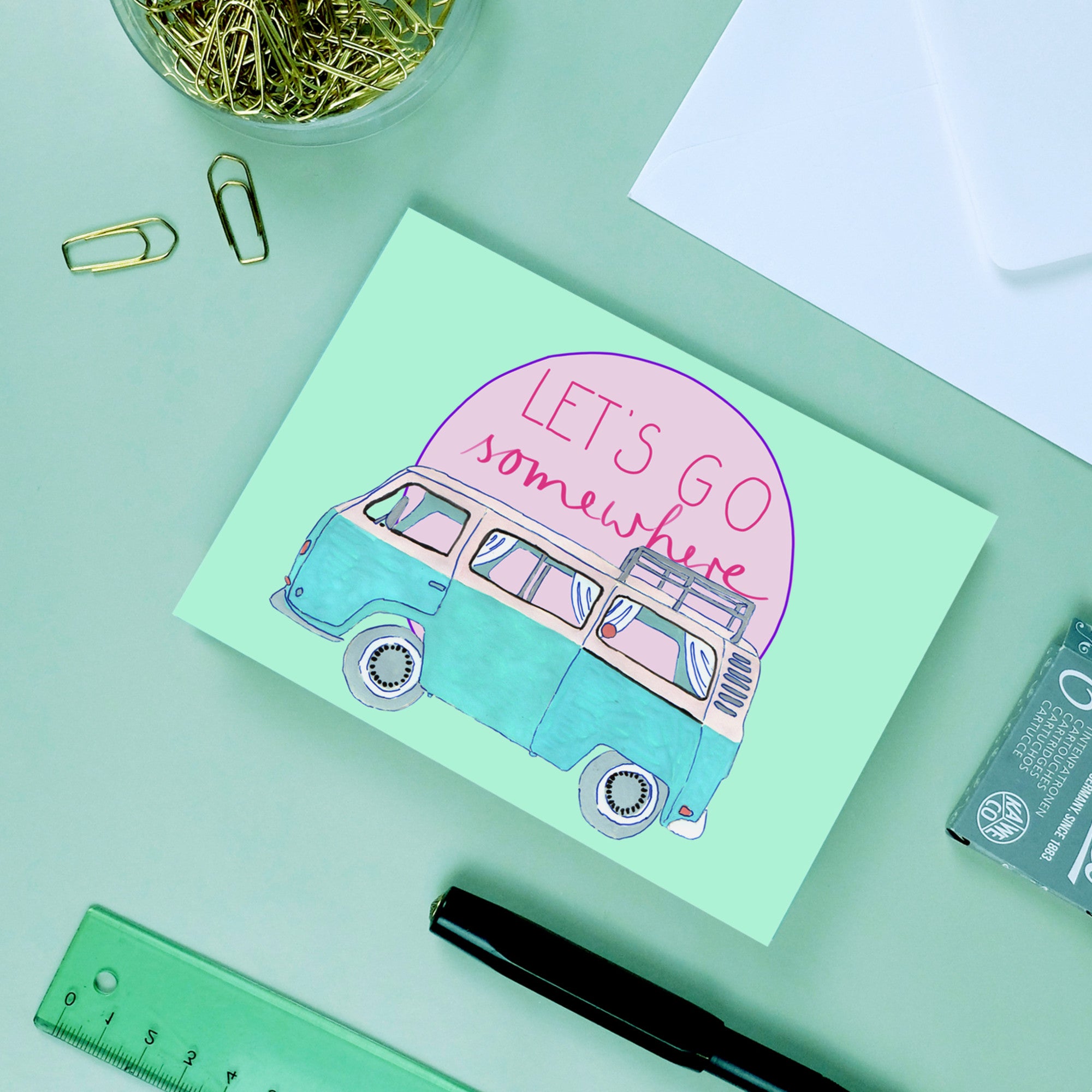 Postkarte mit Zeichnung eines blauen Vans und Text "LET'S GO somewhere", umgeben von Büromaterialien.