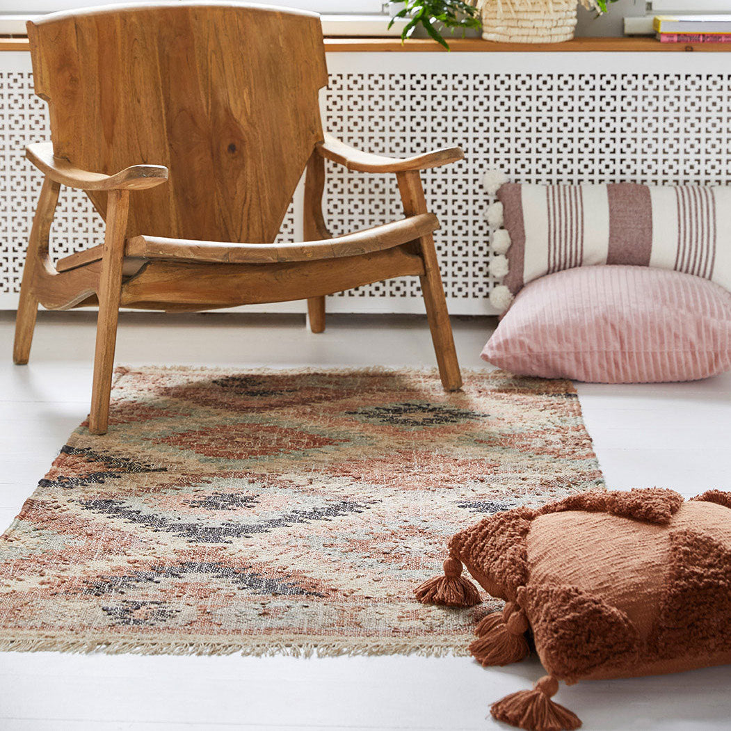 Holzstuhl und dekorative Kissen auf einem gemusterten Teppich in einem wohnlichen Raum.
