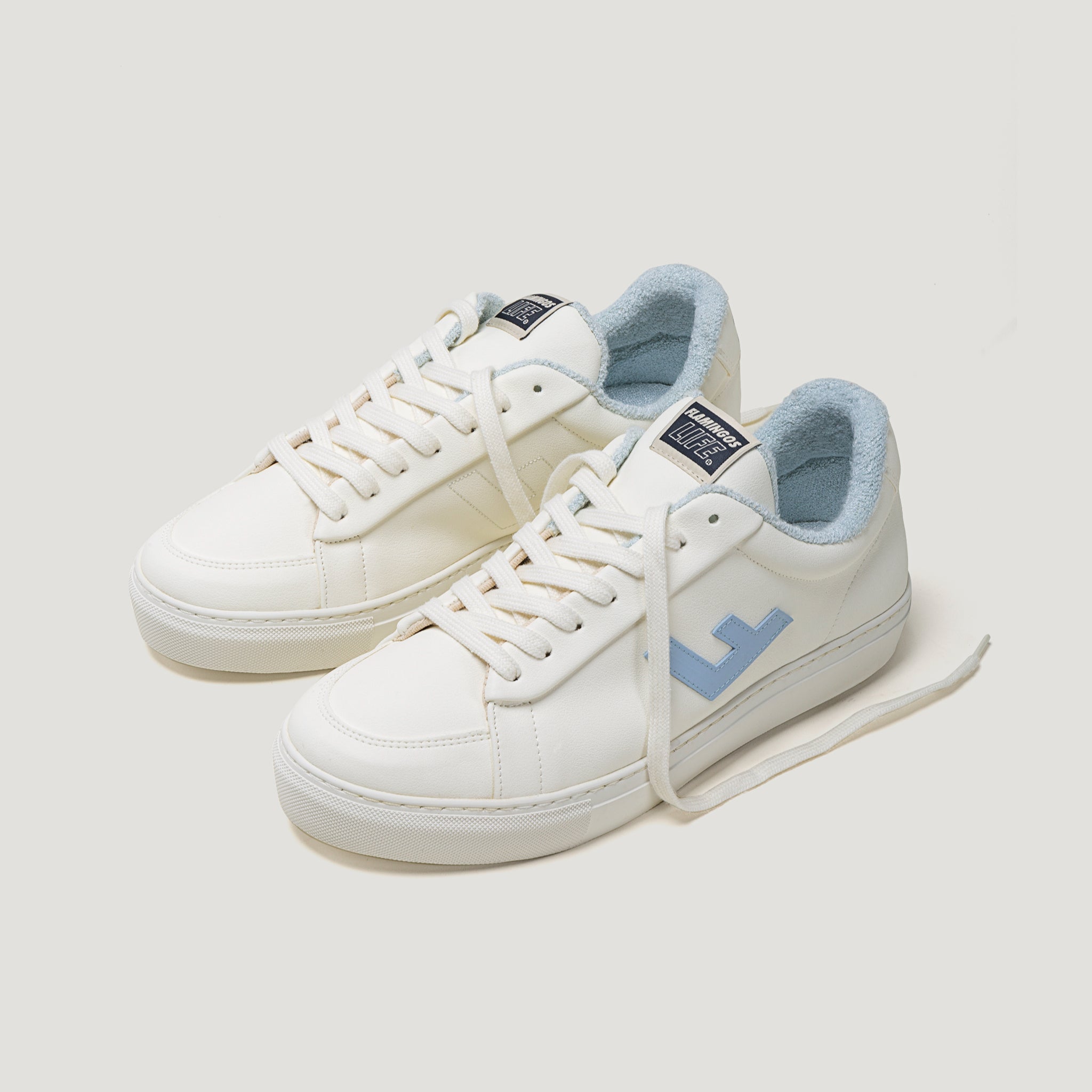 Weiße Sneaker mit blauen Details, hellem Innenfutter und einem Schriftzug auf der Zunge, auf einem weißen Hintergrund.