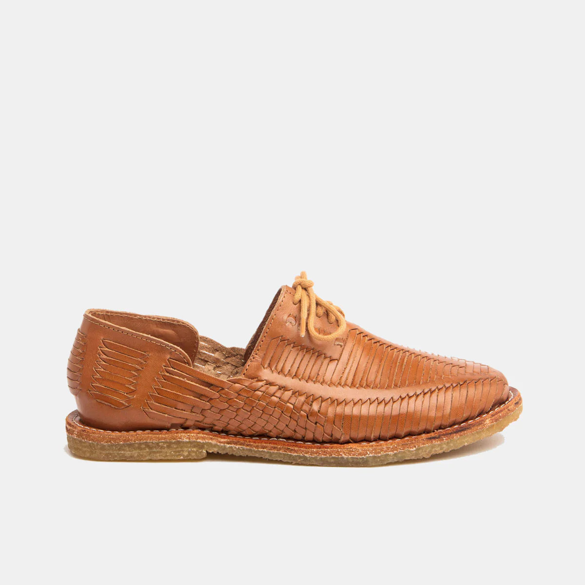 Eine braune Leder-Huarache-Sandale mit gewebten Details, abgerundeter Spitze, hellbraunen Schnürsenkeln und einer flachen, strukturierten Sohle, dargestellt in Profilansicht vor einem schlichten weißen Hintergrund.