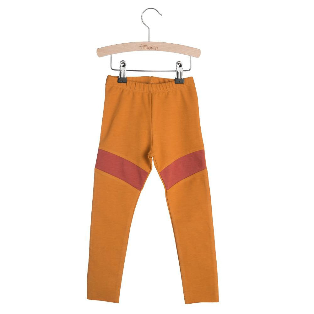 Orangefarbene Kinderleggings mit elastischem Bund und einem diagonalen roten Streifen auf jedem Oberschenkel, ausgestellt auf einem Holzbügel vor weißem Hintergrund.