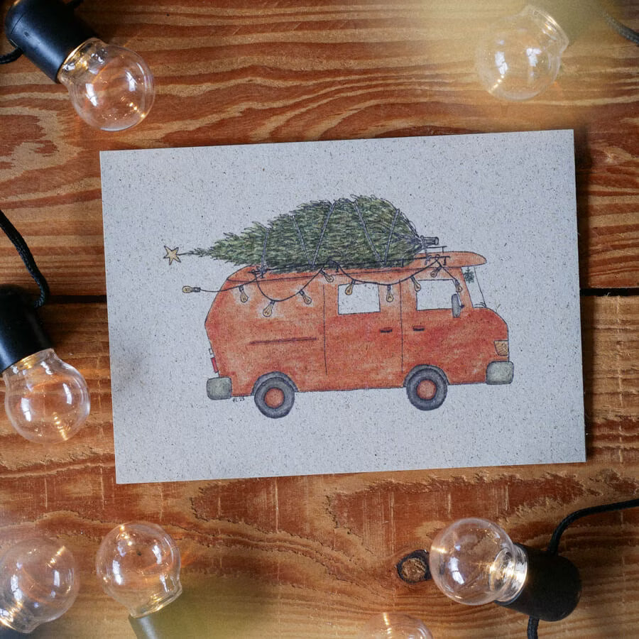 Eine Karte mit einem roten Van, der einen Weihnachtsbaum transportiert, umgeben von Glühbirnen auf einem Holztisch.