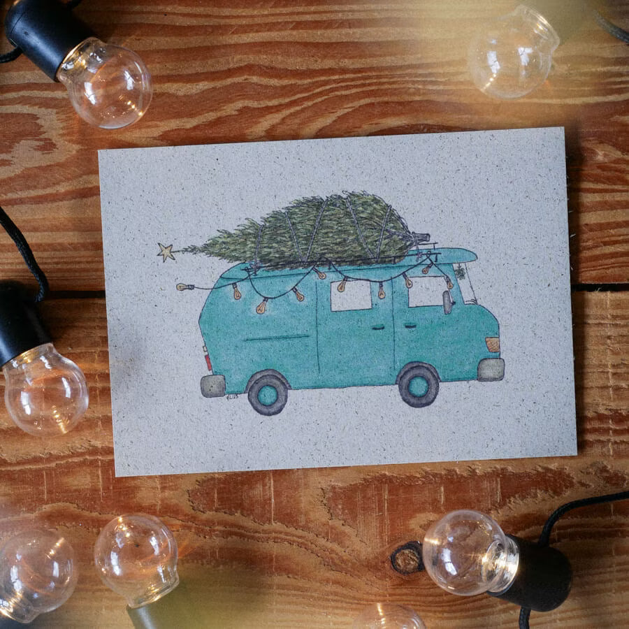 Postkarte mit einem blauen Van, der einen Tannenbaum transportiert, umgeben von Glühbirnen auf Holzhintergrund.