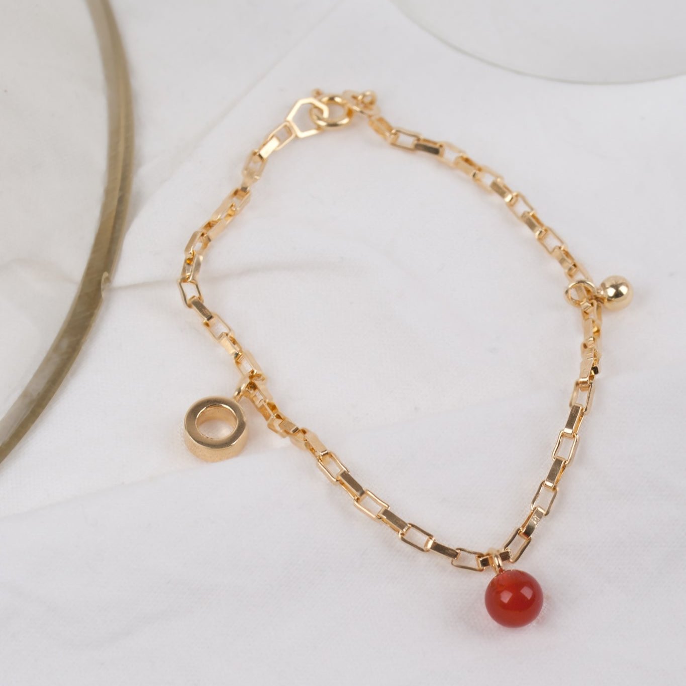 Goldenes Armband mit roten und goldenen Anhängern auf weißem Untergrund.