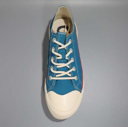 Blauer Sneaker mit weißen Schnürsenkeln und cremefarbener Zehenkappe, vor grauem Hintergrund.