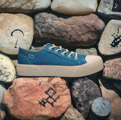 Blauer Sneaker mit weißer Sohle und Schnürsenkeln, auf Steinen mit verschiedenen Symbolen liegend.