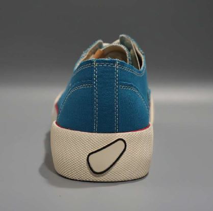 Rückansicht eines blauen Stoffschuhs mit weißer Sohle auf grauem Hintergrund.
