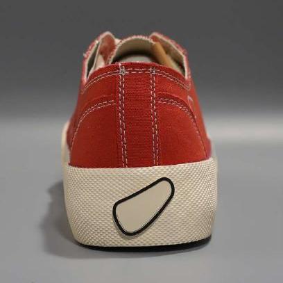 Roter Turnschuh von hinten, mit brauner und beiger Sohle, auf grauem Hintergrund.