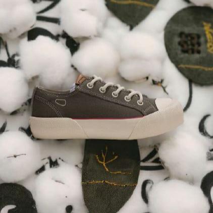 Ein brauner Sneaker liegt auf einer weißen, baumwollartigen Unterlage mit gestickten Mustern.