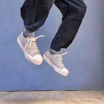 Person springt in der Luft mit weißen Turnschuhen und dunklen Hosen vor blauem Hintergrund.