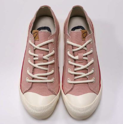 Rosa Sneaker mit weißen Sohlen und Schnürsenkeln, von oben betrachtet, auf grauem Hintergrund.