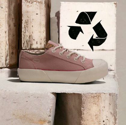 Rosa Sneaker mit weißer Sohle auf Betonblöcken, daneben ein Recycling-Symbol in Schwarz auf weißem Hintergrund.