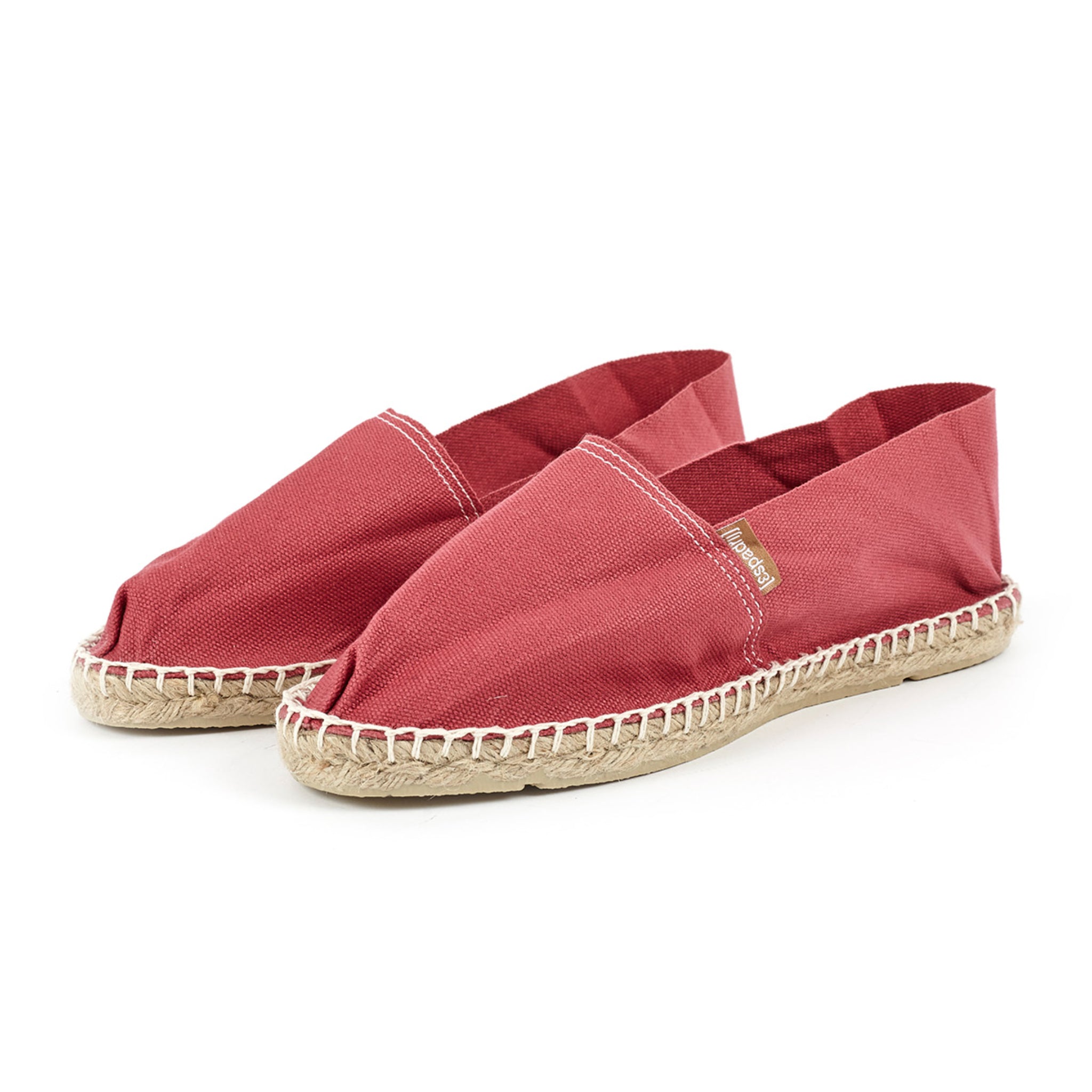 Rote Espadrilles aus Leinen mit flachen, geflochtenen Jutesohlen auf weißem Hintergrund.