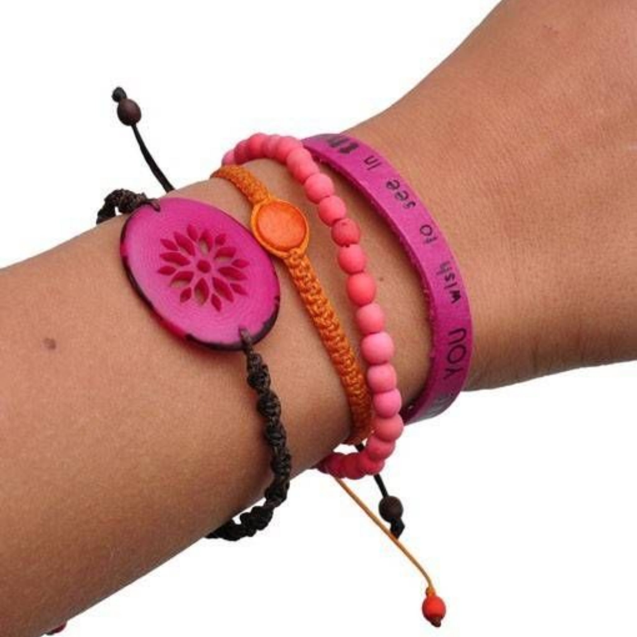 Ein Handgelenk mit mehreren bunten Armbändern, darunter ein rosa Perlenarmband, ein orangefarbenes geflochtenes Armband, ein lila Band mit Text, ein schwarzes Kordelarmband und ein großer rosa Knopf mit Blumenmuster.