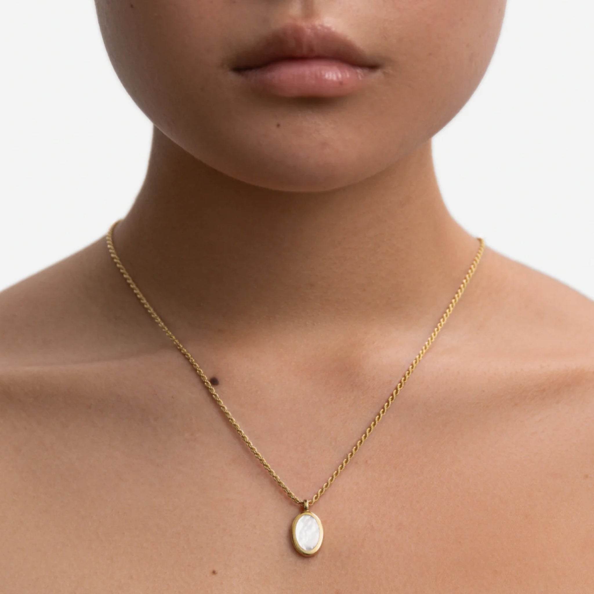 Nahaufnahme eines goldenen Halskettchens mit ovalem Anhänger an einem Hals vor weißem Hintergrund.
